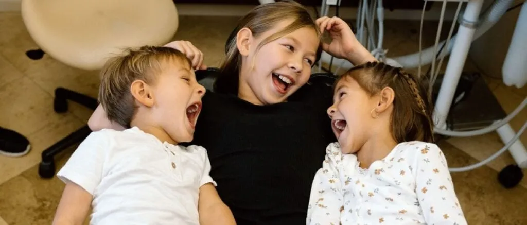 Three children laughing and enjoying each other's company in a dental office setting, promoting a positive and friendly atmosphere for dental visits.